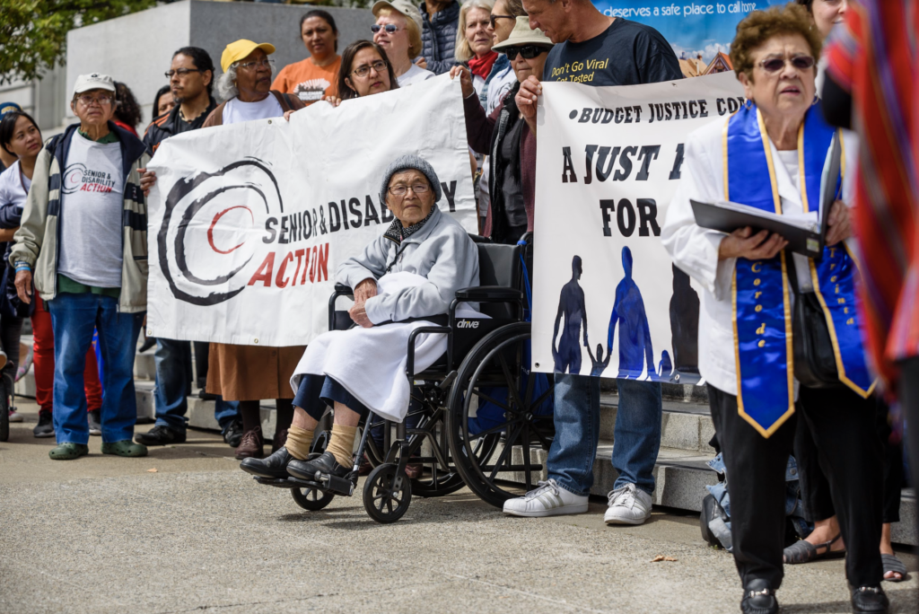 Advocates surround a Senior & Disability Action and a Budget Justice banner